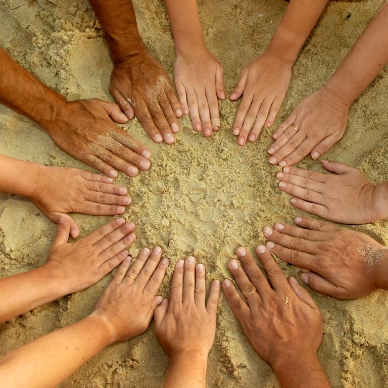 Hände, die zusammen einen Kreis auf einem Sandplatz bilden